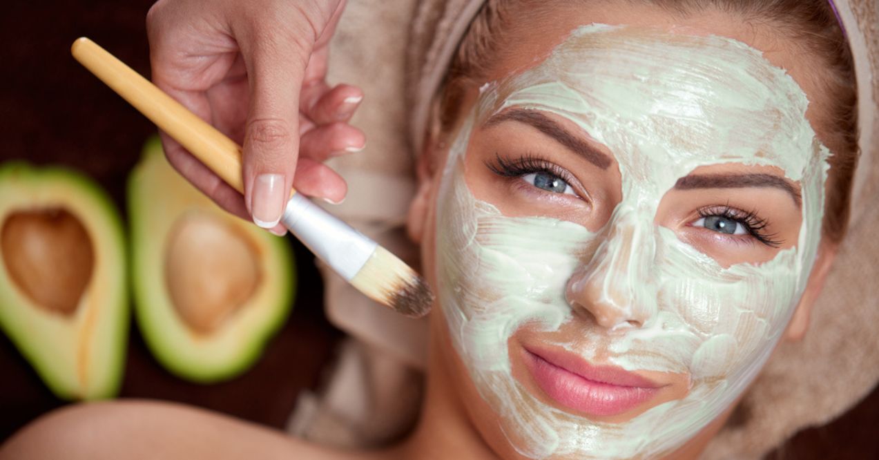 A woman with an avocado face mask being applied with a brush