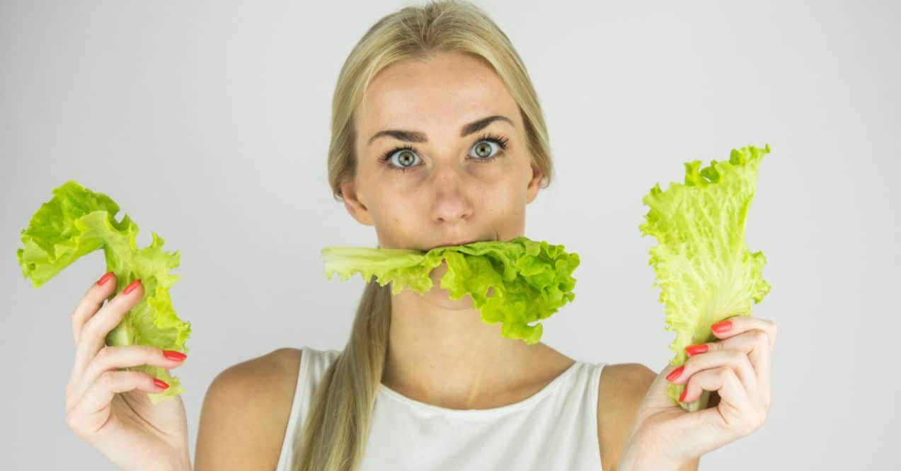 A woman holding lettuce leaves in both hands with a piece of lettuce in her mouth