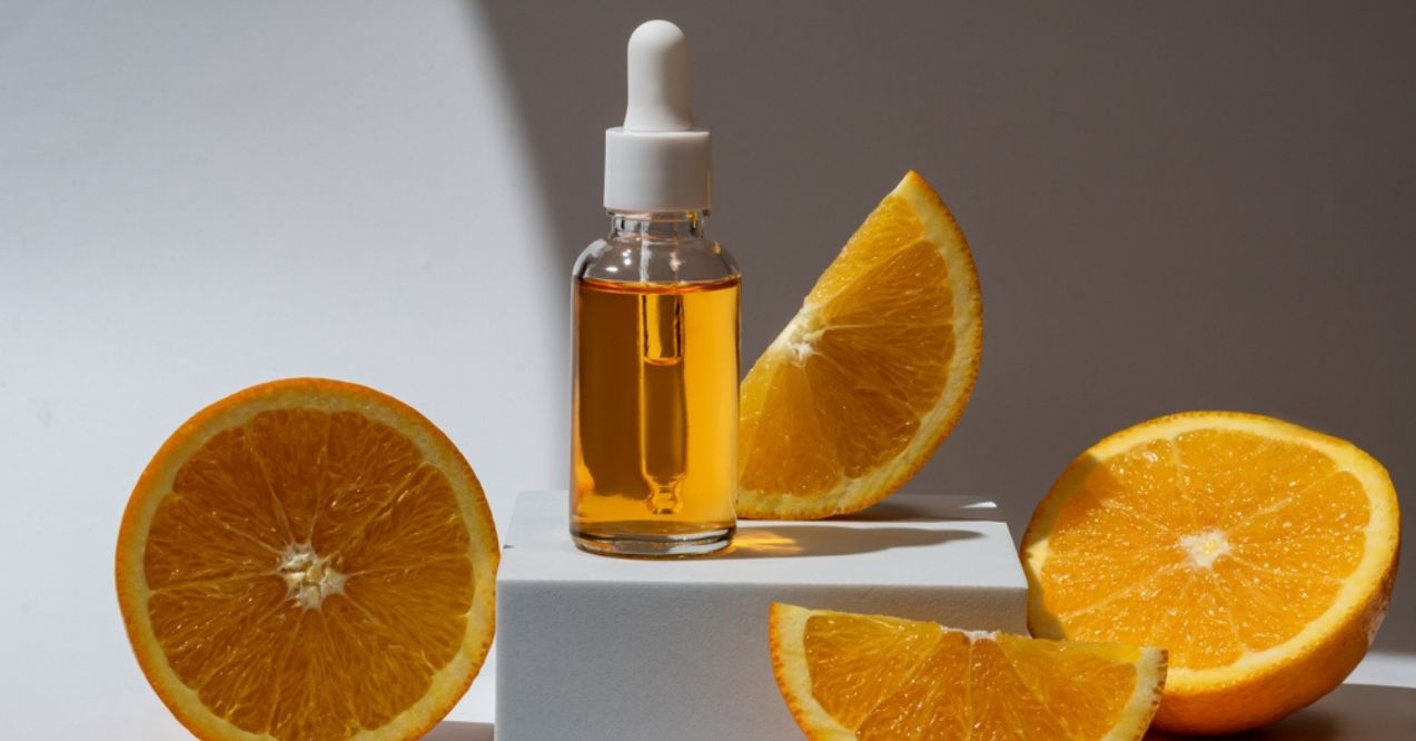 A bottle of vitamin C serum surrounded by fresh orange slices