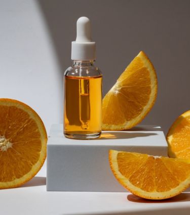 A bottle of vitamin C serum surrounded by fresh orange slices