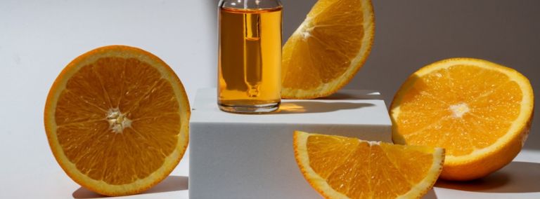 A bottle of vitamin C serum surrounded by fresh orange slices