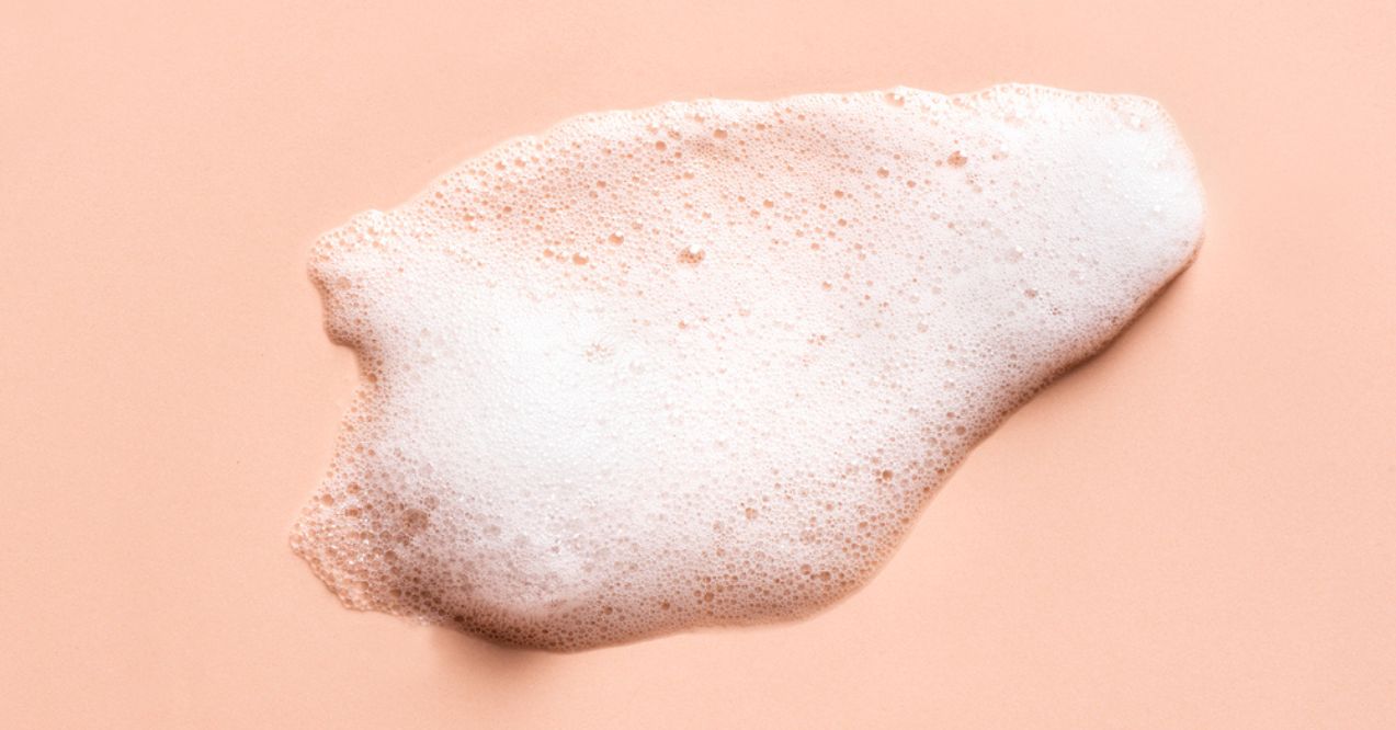 A smear of foamy face cleansing mousse on a peach-colored background