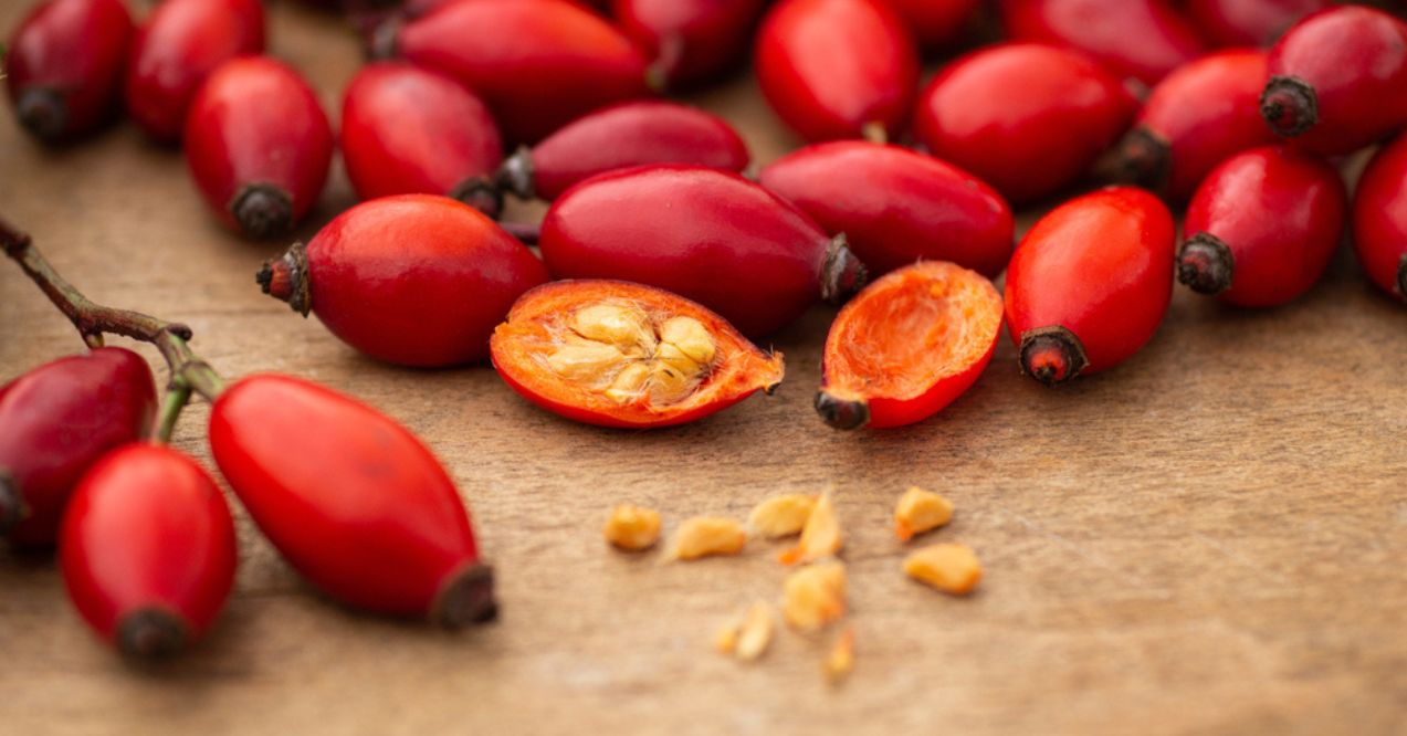 Freshly picked rose hips, some cut open to reveal seeds, on a wooden surface