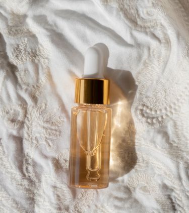 A small bottle of retinol with a golden cap, placed on a white textured fabric