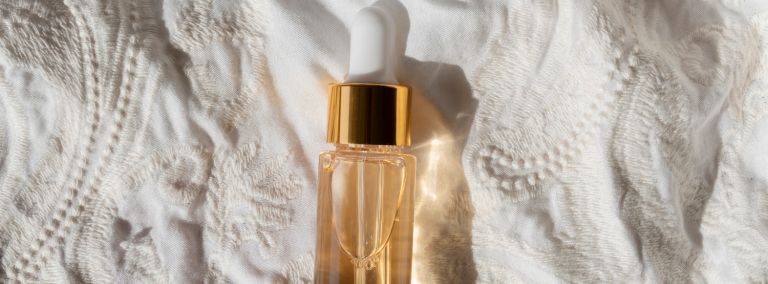 A small bottle of retinol with a golden cap, placed on a white textured fabric