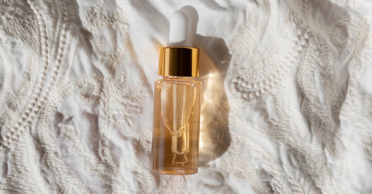 A small bottle of retinol with a golden cap, placed on a white textured fabric