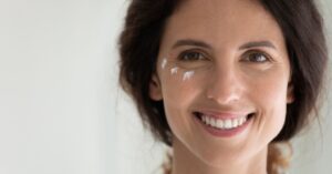 A smiling woman with small dabs of skincare cream under her right eye