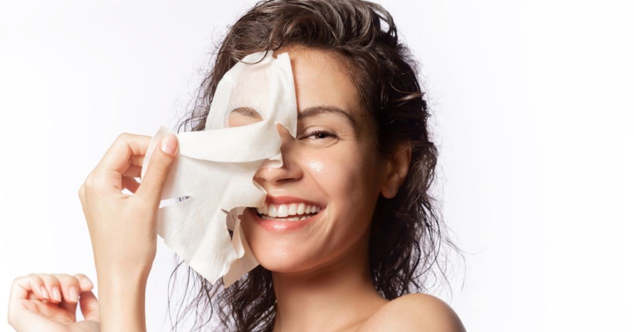 Smiling woman removing a hydrating face mask sheet