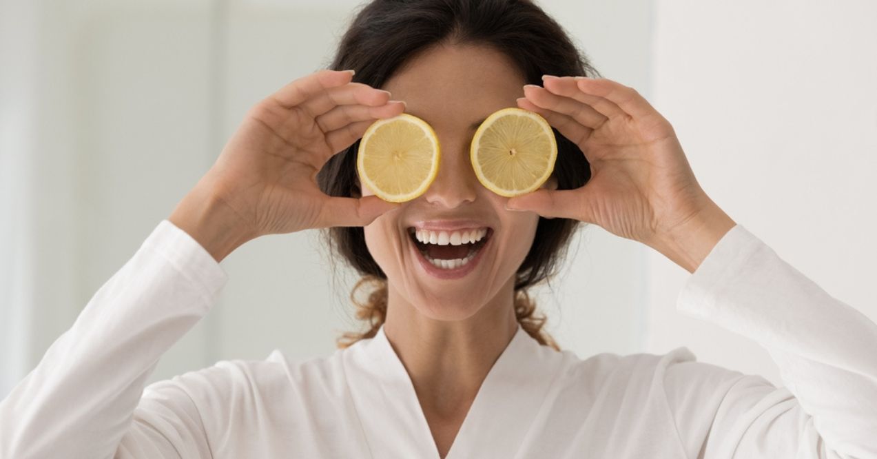 A smiling woman holding lemon slices in front of her eyes