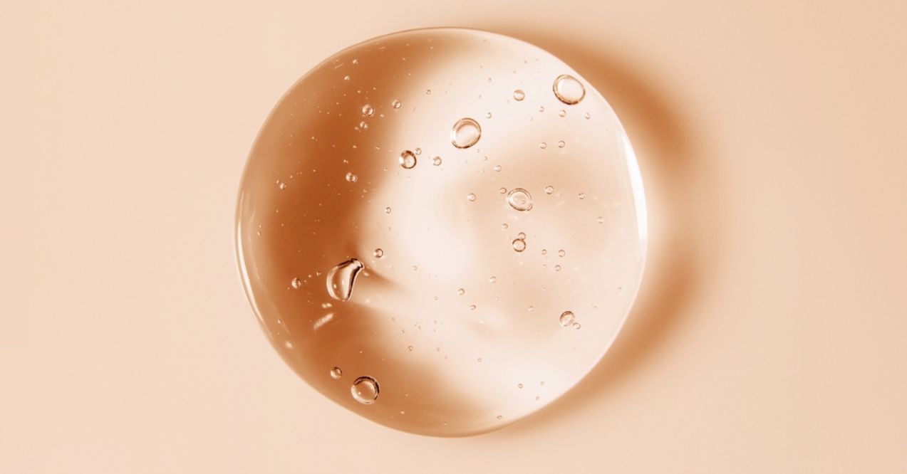 A clear droplet of serum with air bubbles on a peach-colored background