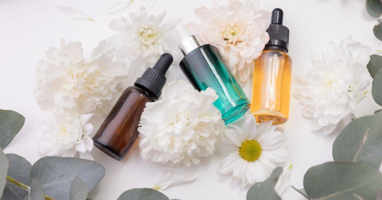 Three dropper bottles of skincare products surrounded by white flowers and eucalyptus leaves