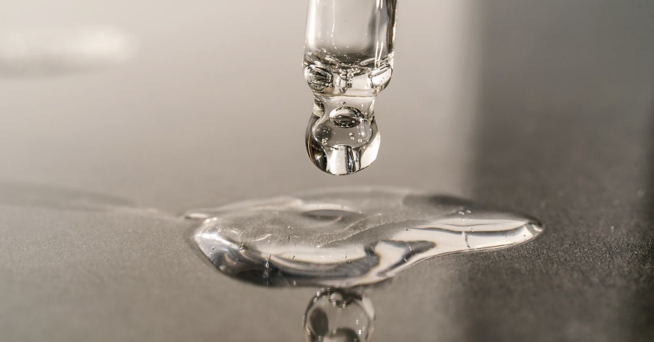 A close-up image of a dropper releasing a droplet of retinol onto a smooth surface