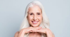 A smiling older woman with long white hair, resting her chin on her hands