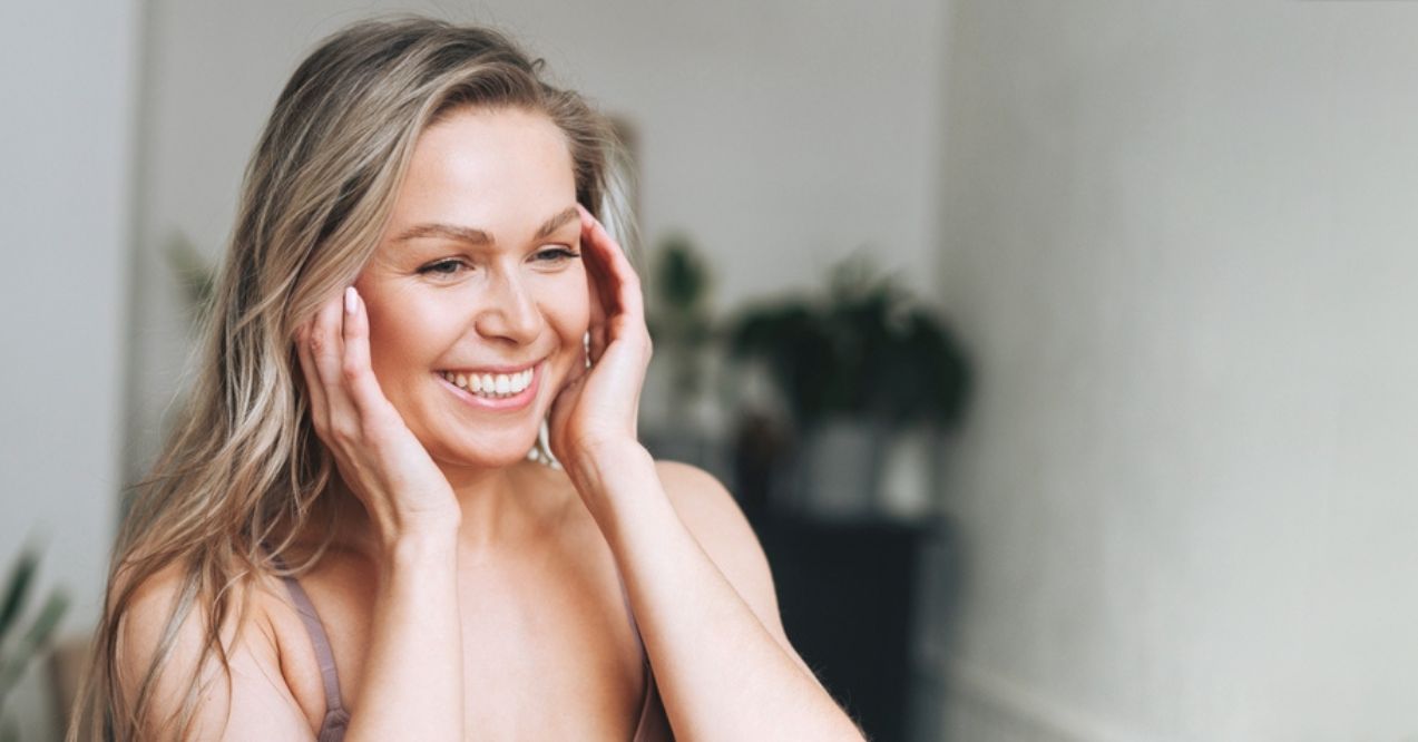 A blonde woman smiling with her hands gently touching her face