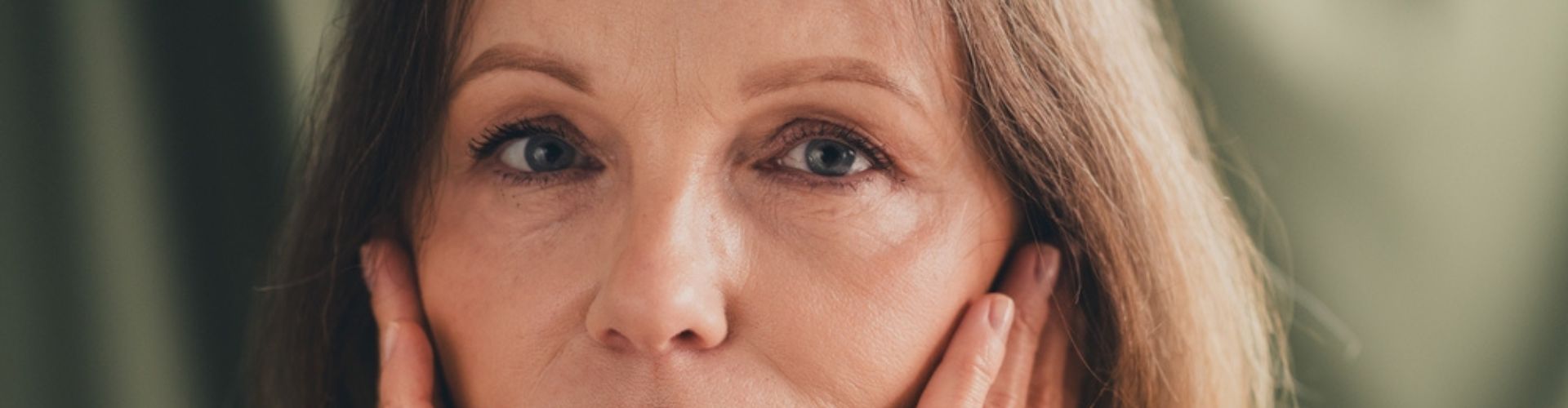 A woman with short hair gently touching her face with both hands