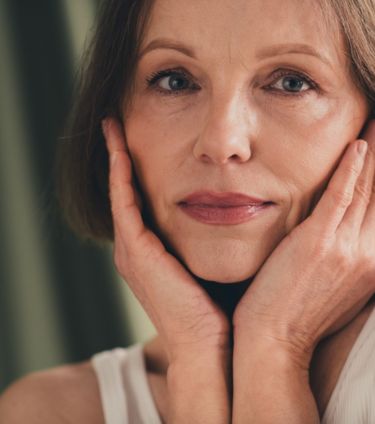 A woman with short hair gently touching her face with both hands