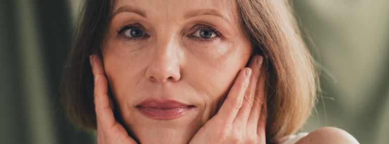 A woman with short hair gently touching her face with both hands