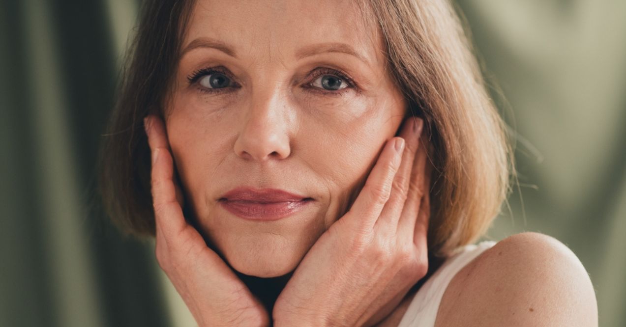 A woman with short hair gently touching her face with both hands