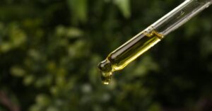 Close-up of a dropper with golden oil and green foliage background