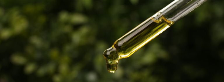 Close-up of a dropper with golden oil and green foliage background