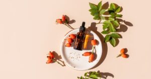 Rosehip oil bottle with rosehip berries and leaves on a white plate