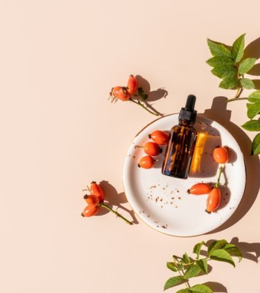 Rosehip oil bottle with rosehip berries and leaves on a white plate