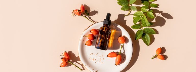 Rosehip oil bottle with rosehip berries and leaves on a white plate