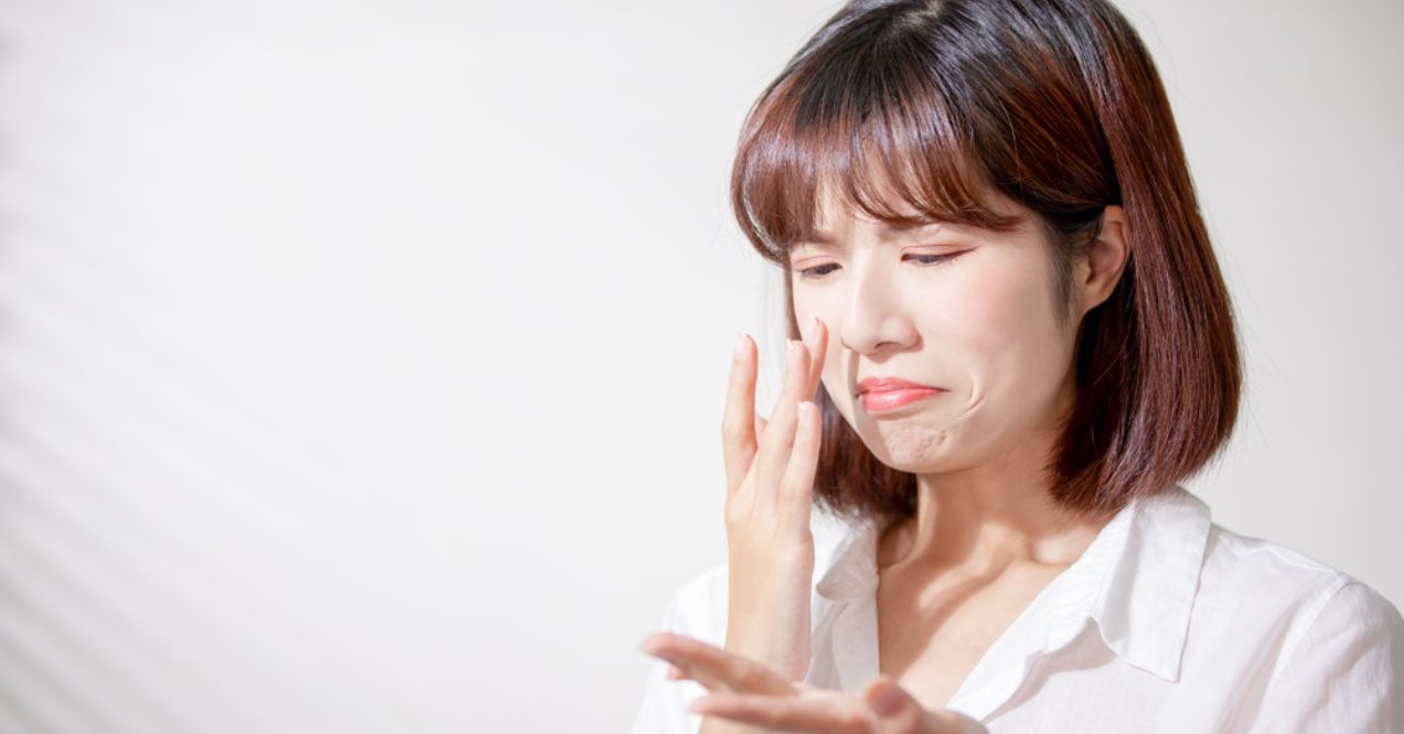 An Asian woman with a sad expression, touching her face with one hand