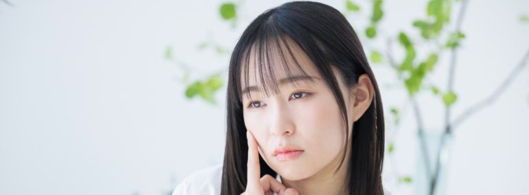 A young woman with long dark hair, touching her face with a thoughtful expression