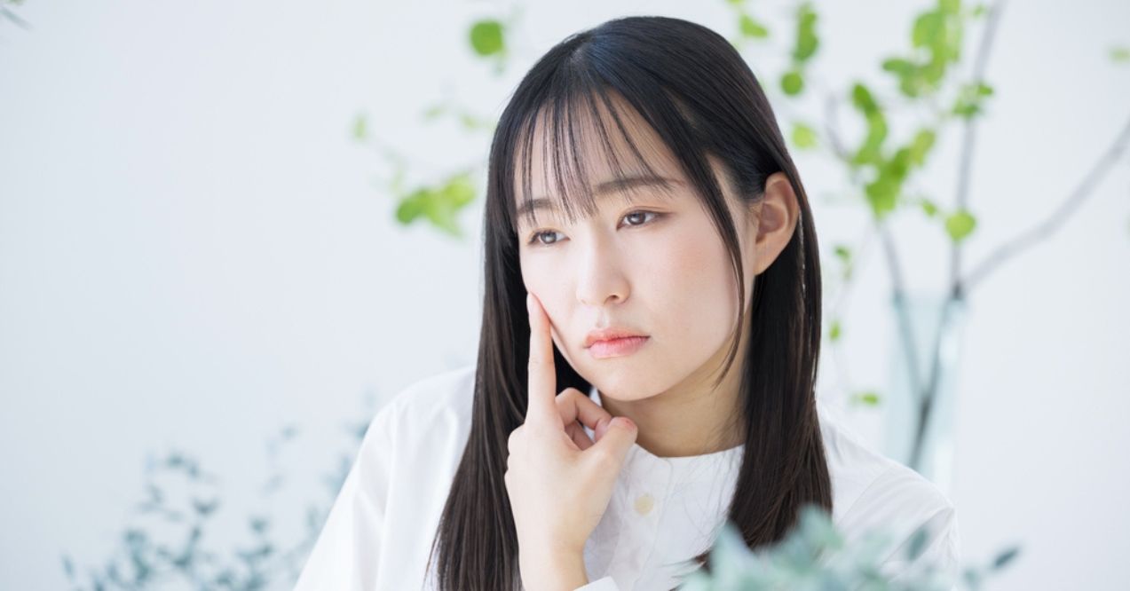 A young woman with long dark hair, touching her face with a thoughtful expression