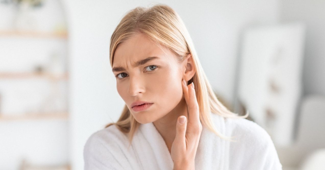 A woman with a concerned expression touching her face while looking in the mirror