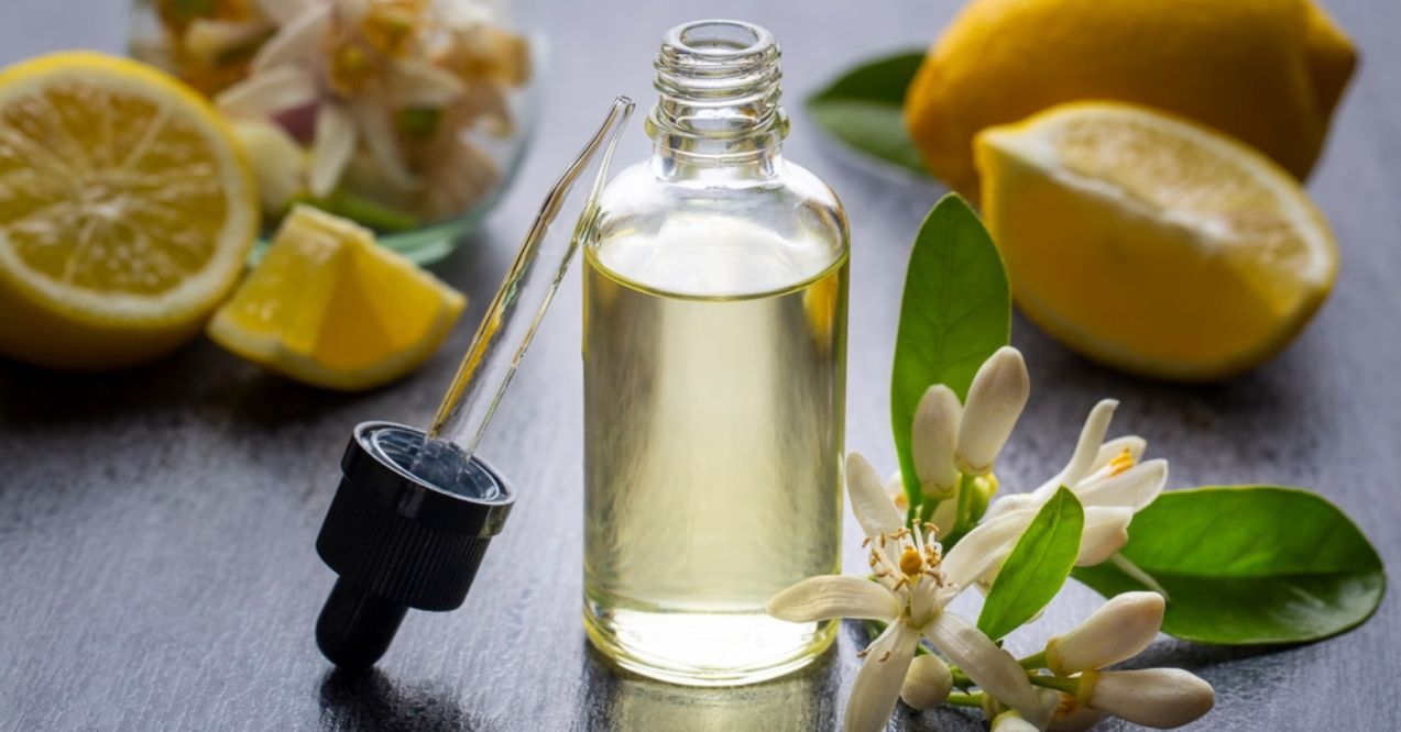 A glass bottle of lemon essential oil with a dropper, surrounded by fresh lemon slices