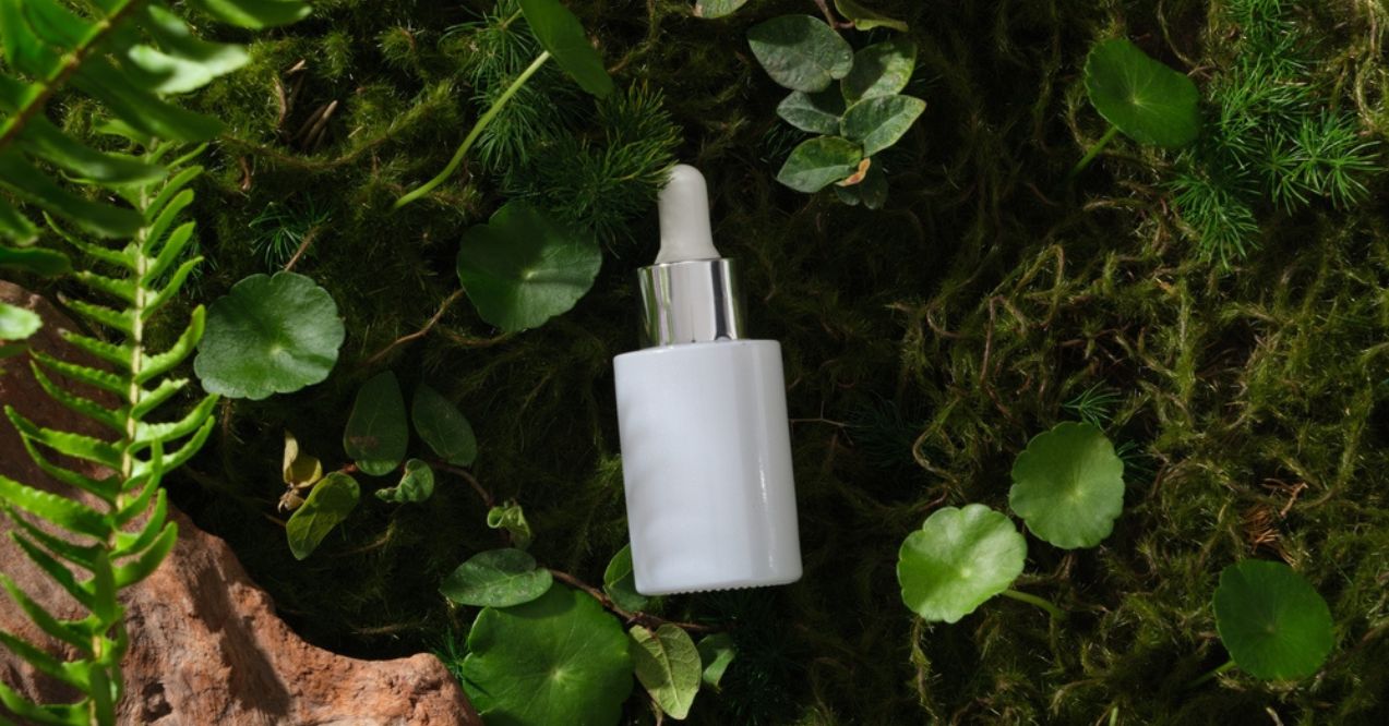 A dropper bottle with a white cap placed on a bed of green leaves and moss