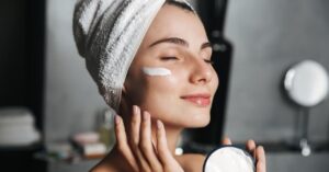 Woman applying face cream with a towel wrapped around her head