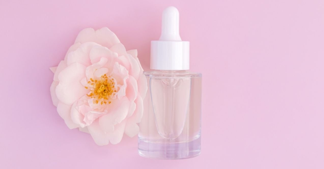  clear dropper bottle with a white cap placed next to a light pink flower