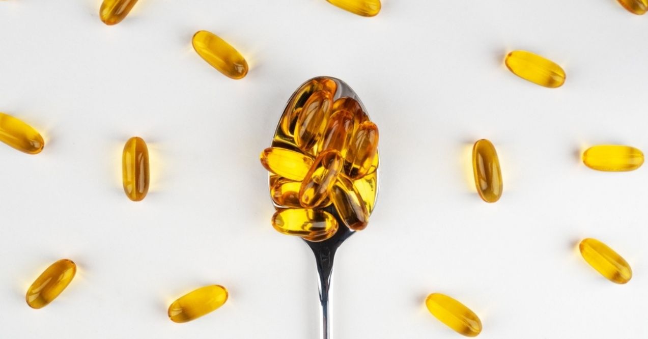 Spoon filled with omega-3 capsules surrounded by scattered capsules