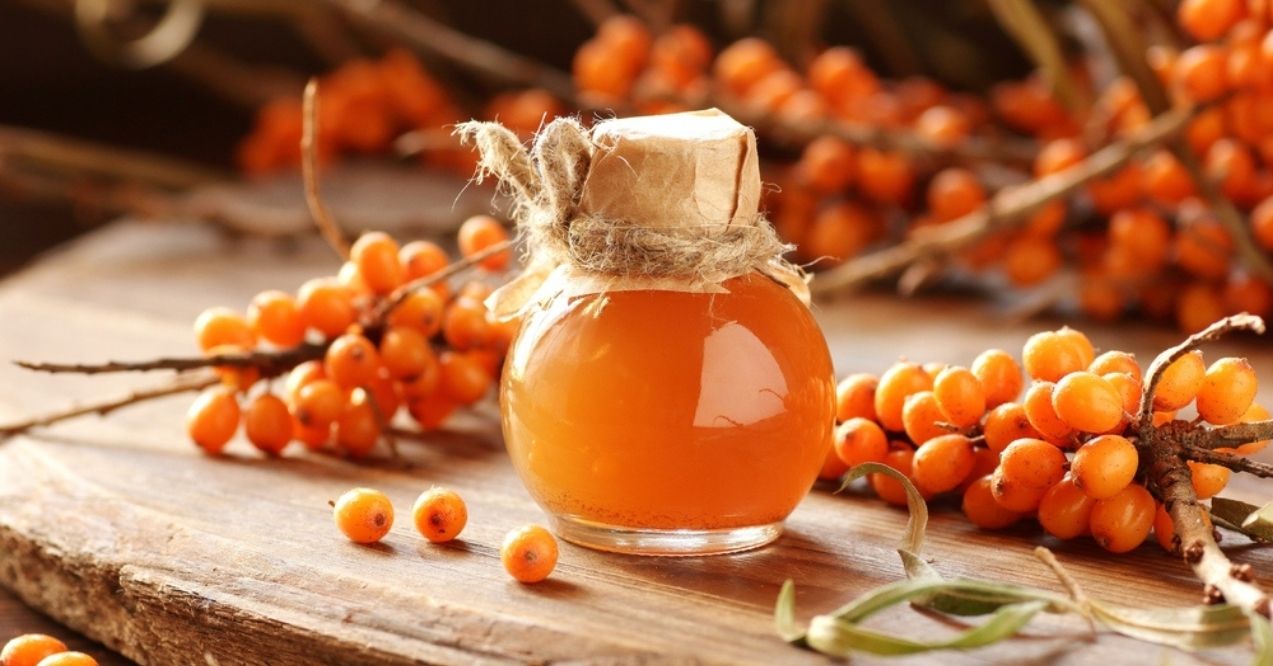 Glass bottle of sea buckthorn oil surrounded by sea buckthorn berries on a wooden surface