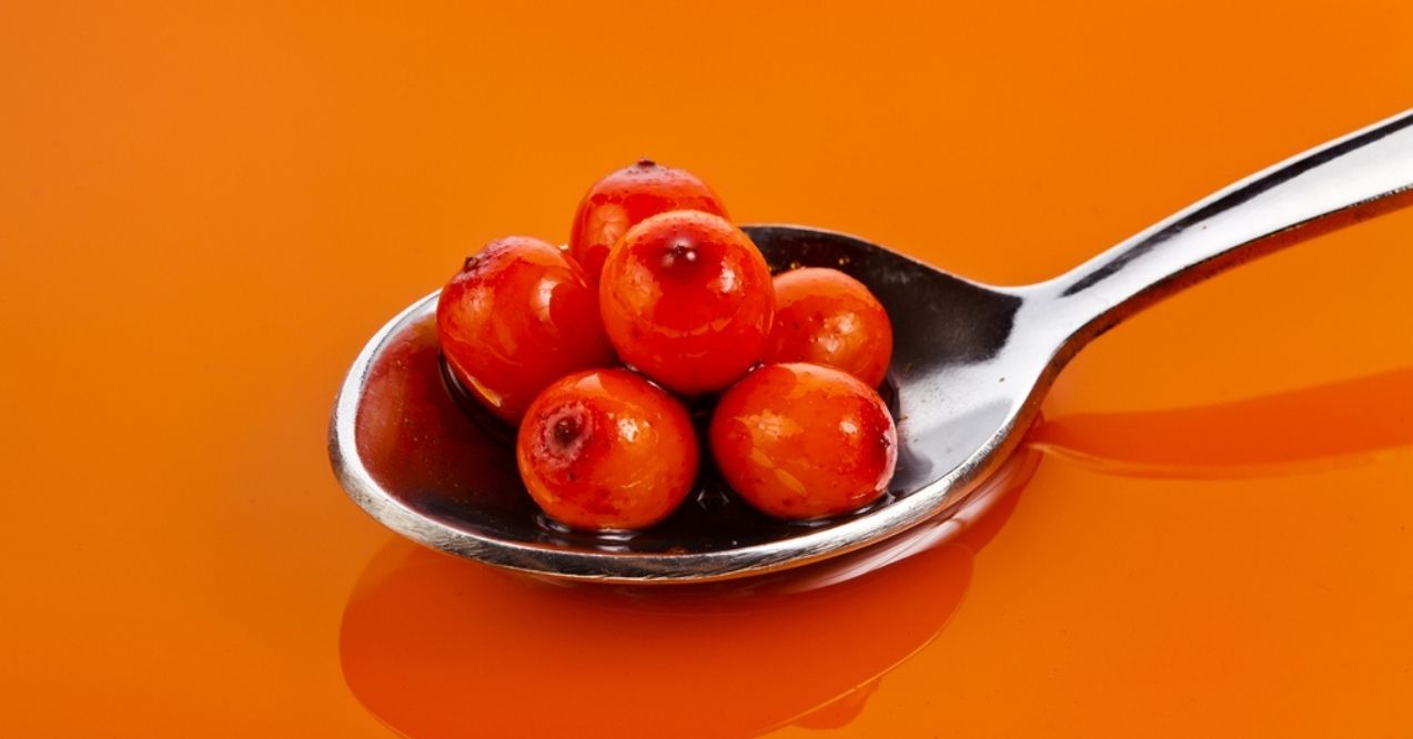 Sea buckthorn berries on a spoon against an orange background