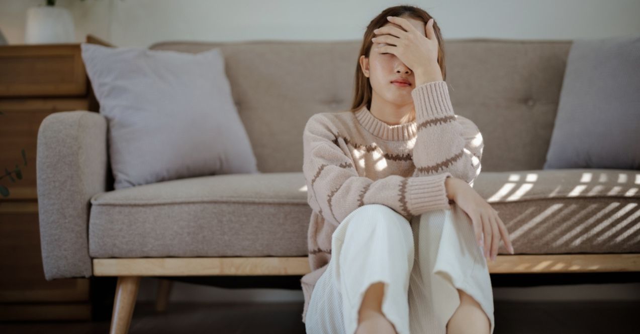 Woman sitting on the floor with hand on her face, appearing stressed