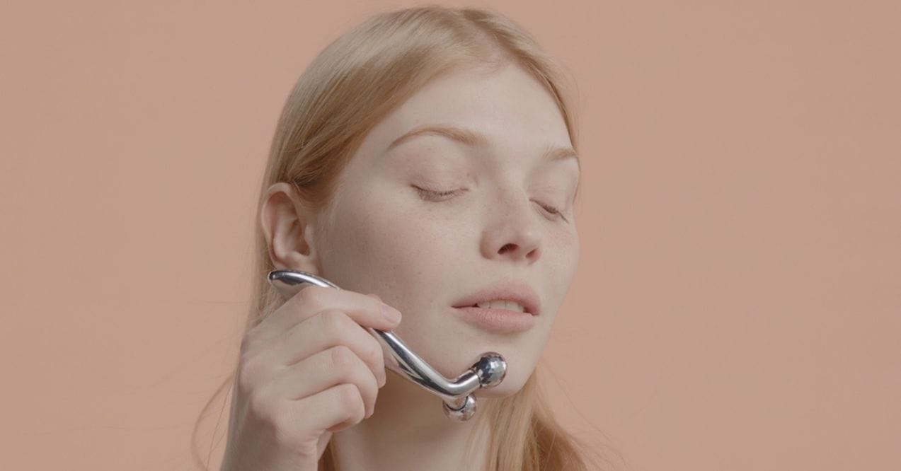 Woman using a metal face roller on her cheek