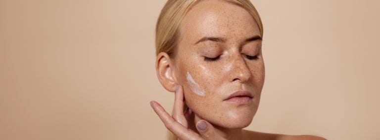 Woman applying cream to her cheek with closed eyes