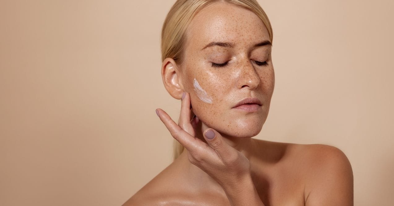 Woman applying cream to her cheek with closed eyes