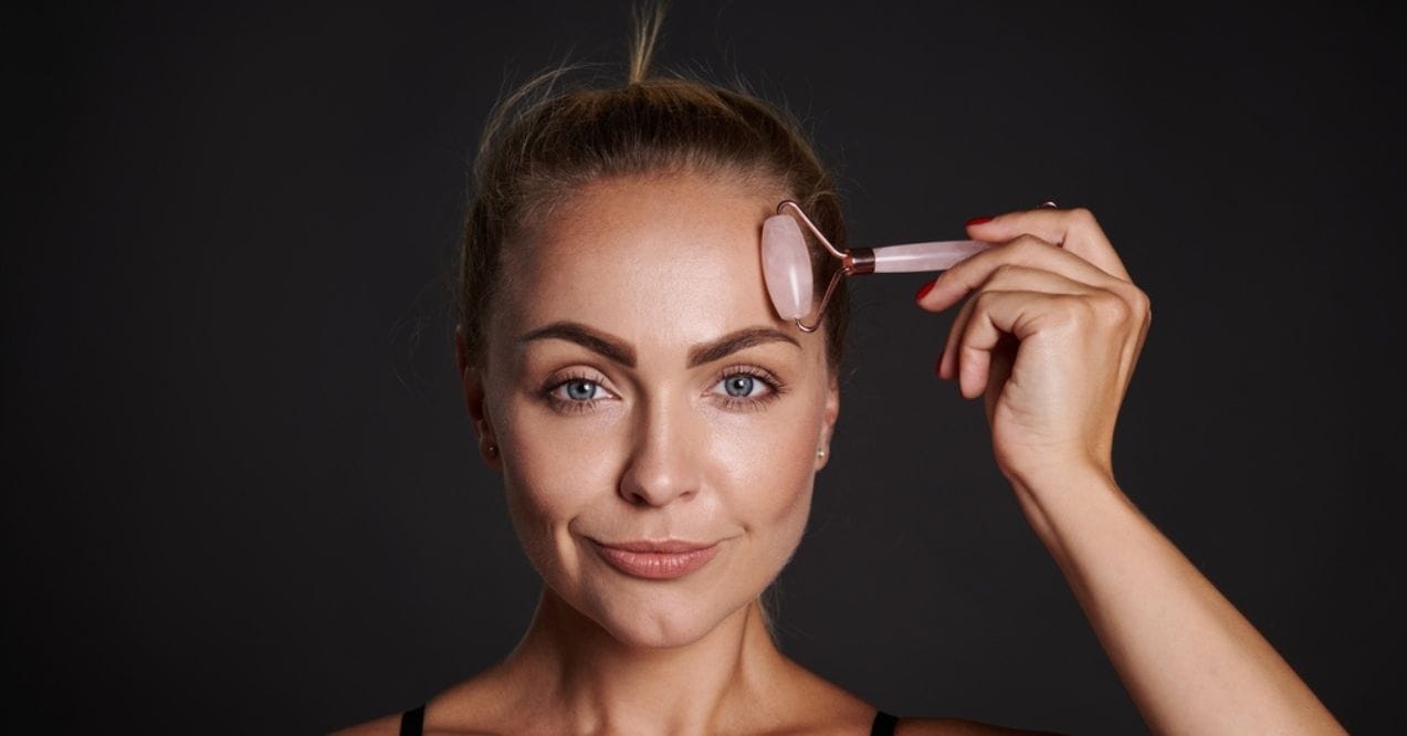 Woman using a rose quartz face roller on her forehead