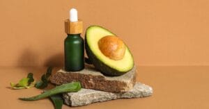 Avocado oil bottle with half avocado, leaves, and aloe vera on stacked stones