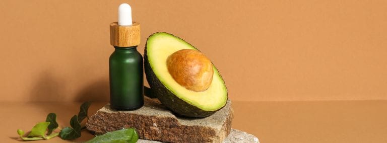 Avocado oil bottle with half avocado, leaves, and aloe vera on stacked stones