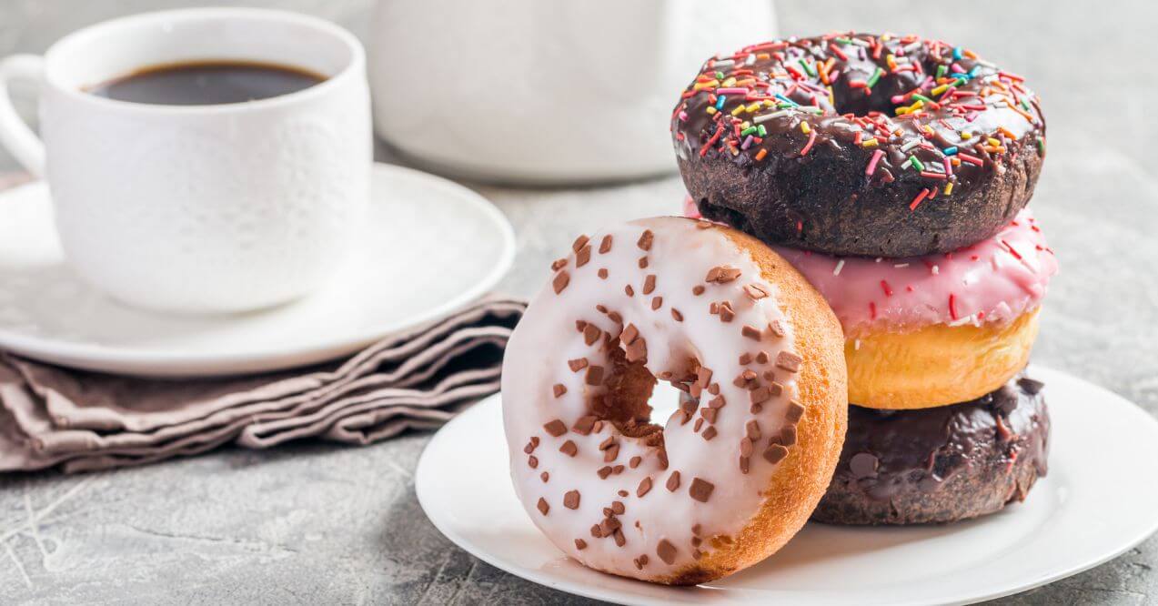 Plate of assorted donuts with a cup of coffee on the side.