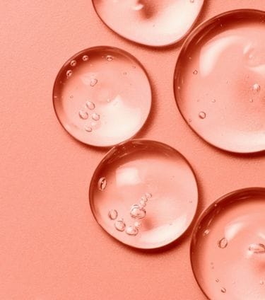 Close-up of translucent gel droplets on a peach-colored background