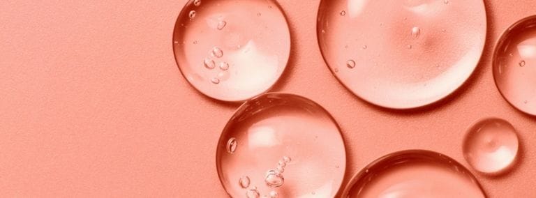 Close-up of translucent gel droplets on a peach-colored background