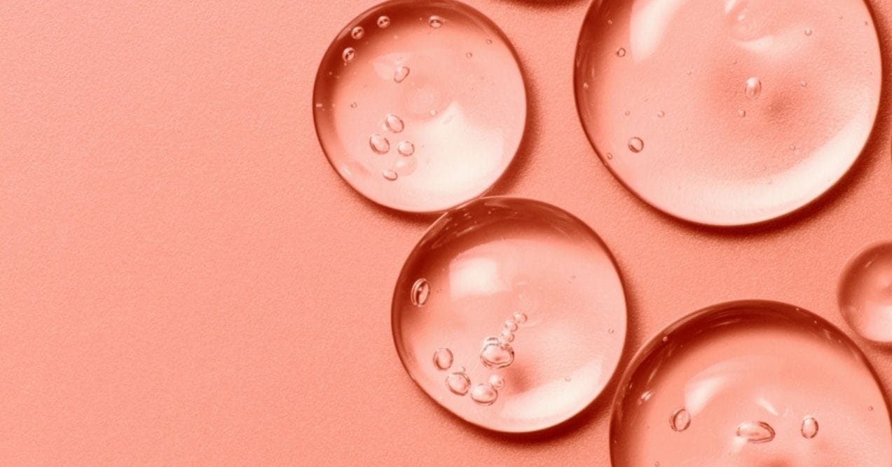 Close-up of translucent gel droplets on a peach-colored background