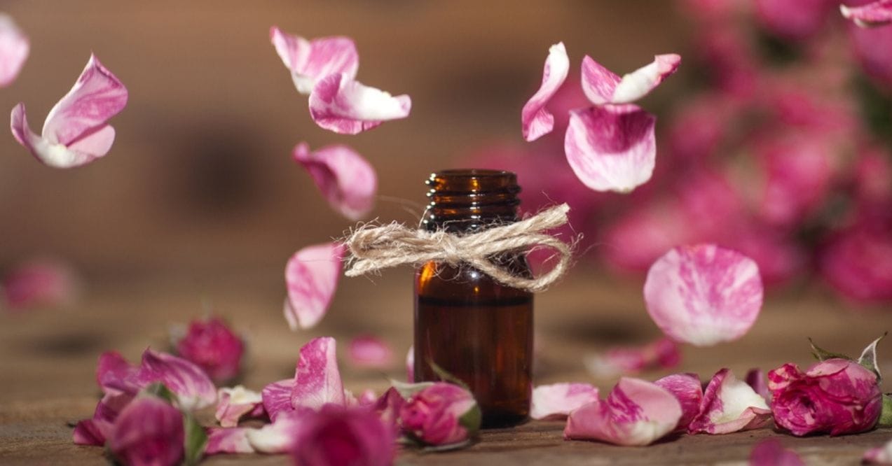 Amber glass bottle of rose oil surrounded by floating pink rose petals